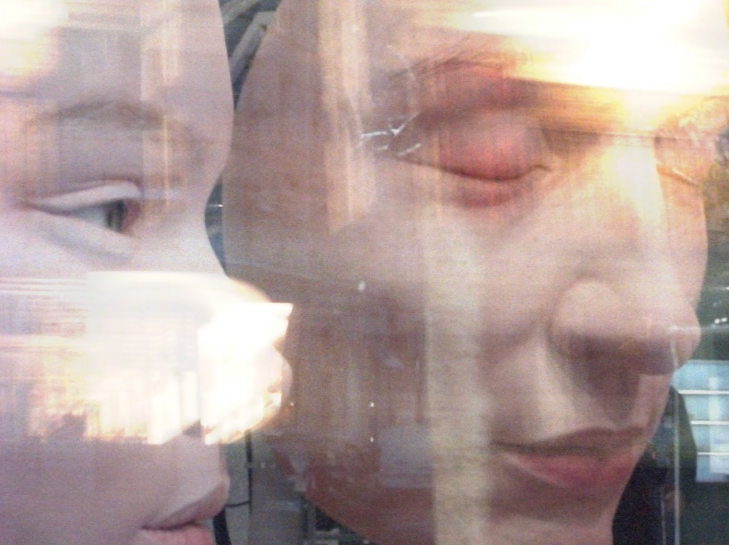Two faces overlaid and semi-transparent — one in profile with lowered eyes, one larger with eyes closed — layered over reflections of a street and a bright flare of light.